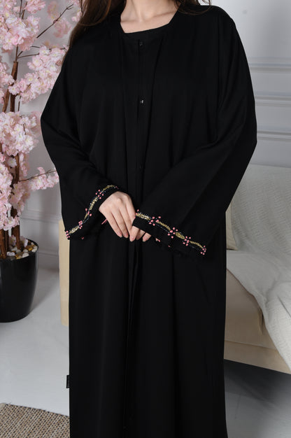 An abaya with pink and gold accents on black crepe fabric