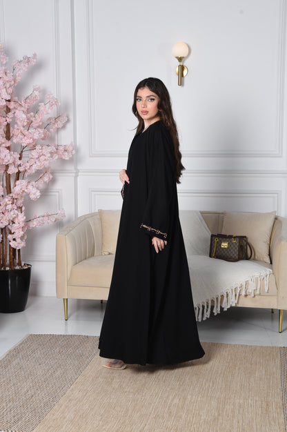 An abaya with pink and gold accents on black crepe fabric