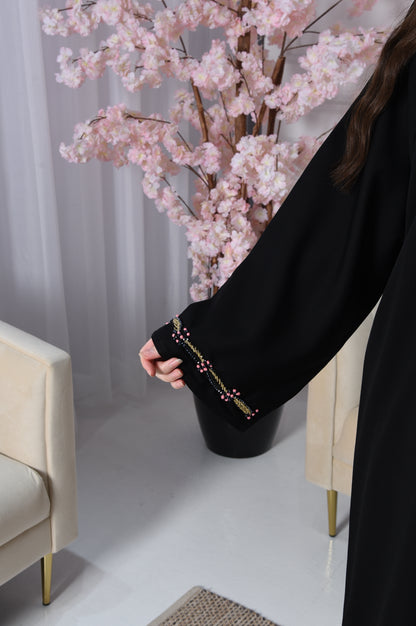 An abaya with pink and gold accents on black crepe fabric